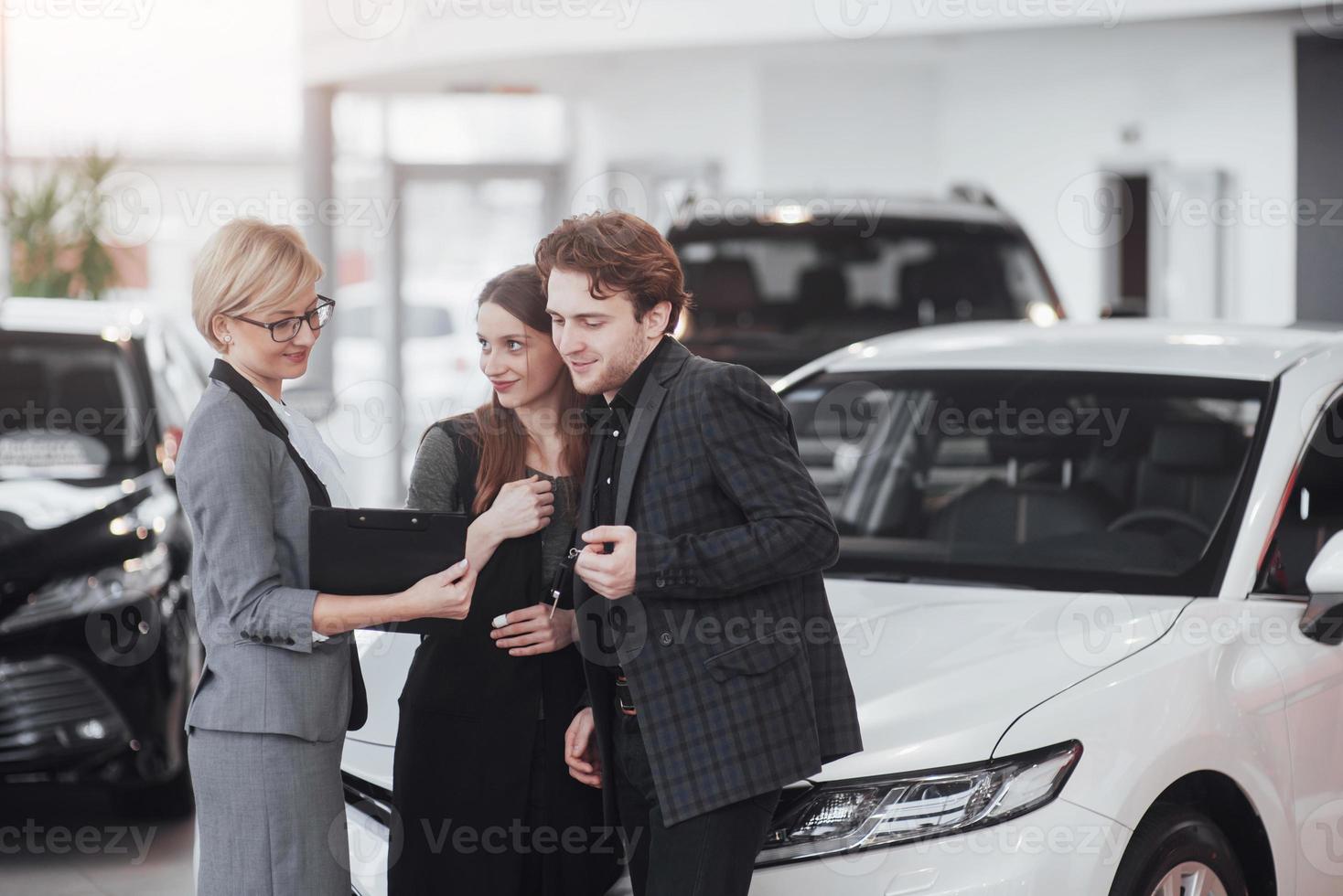 klaar om te rijden. prachtig verliefde paar poseren samen in de buurt van hun nieuwe auto bij de autodealer showroom salon glimlachend gelukkig tonend hun autosleutels vervoer voertuig verhuur kopen welzijn levensstijl foto