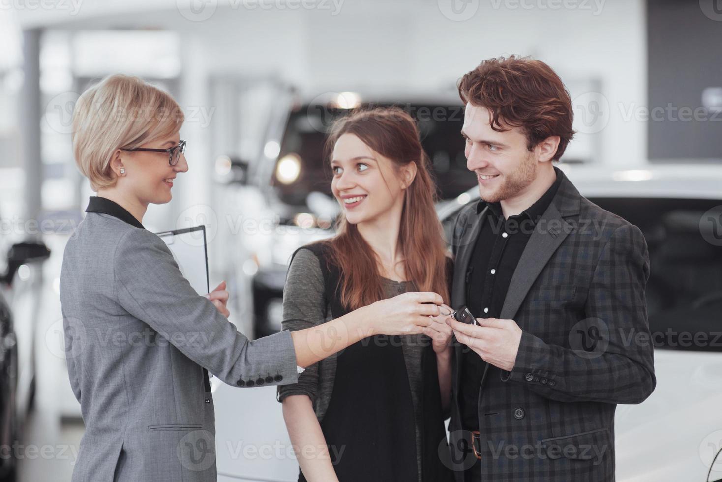 samen hun eerste auto kopen. hoge hoekmening van jonge autoverkoper die bij de dealer staat en de klanten vertelt over de kenmerken van de auto foto