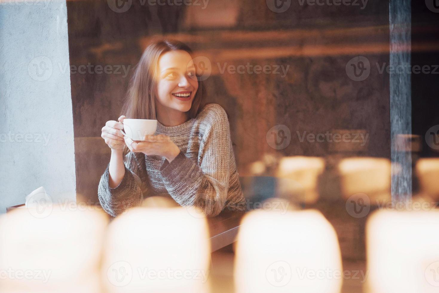 mooie jonge vrouw die geniet van koffiecappuccino met schuim bij het raam in een café foto
