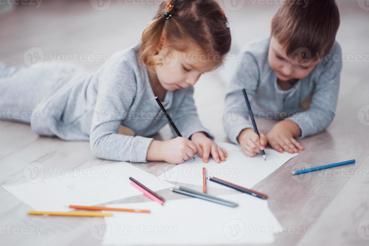 kinderen liggen in pyjama op de grond en tekenen met potloden. schattig kind schilderen met potloden foto