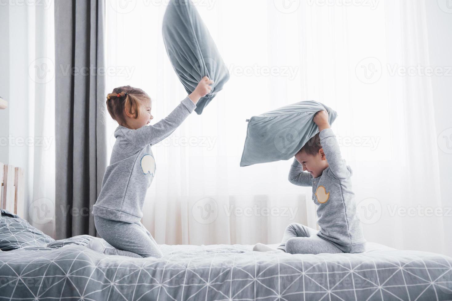 kleine jongen en meisje voerden een kussengevecht op het bed in de slaapkamer. stoute kinderen slaan elkaar met kussens. ze houden van dat soort spel foto