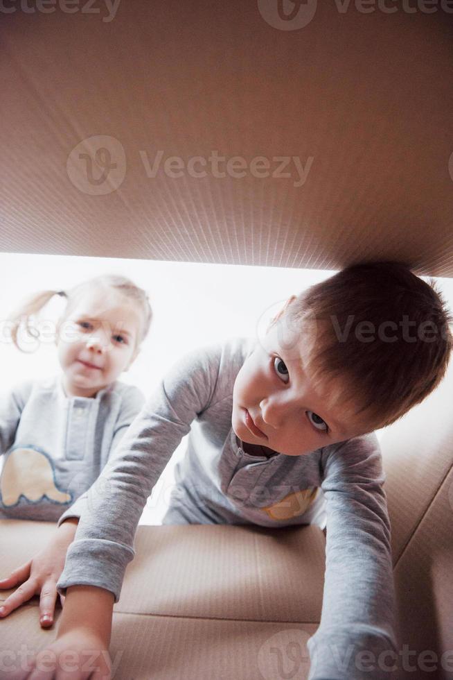 twee kleine jongens en meisjes die een kartonnen doos openen en er middenin klimmen. kinderen hebben plezier foto