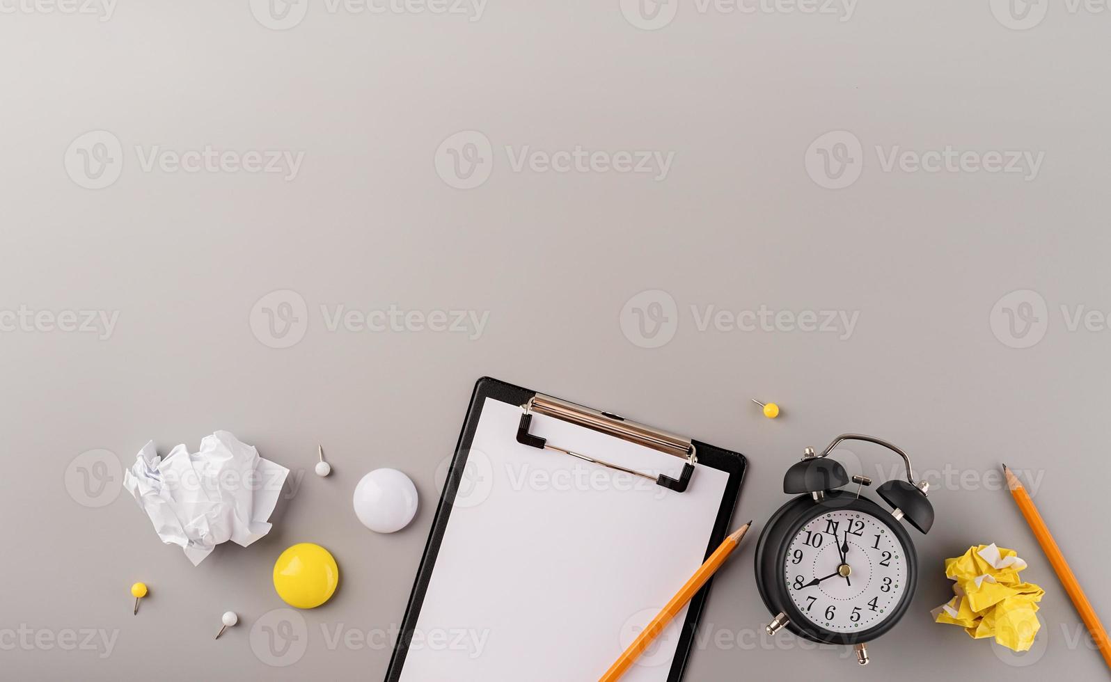 blanco papier op klembord, witte wekker en briefpapier bovenaanzicht op grijze achtergrond foto