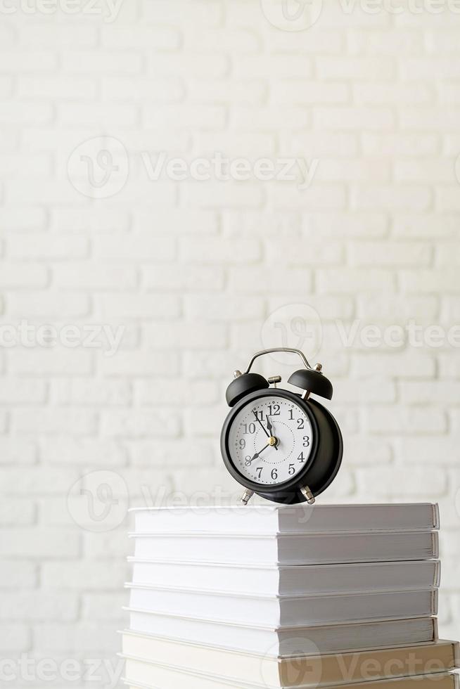 zwarte wekker op stapel boeken op witte bakstenen muurachtergrond foto