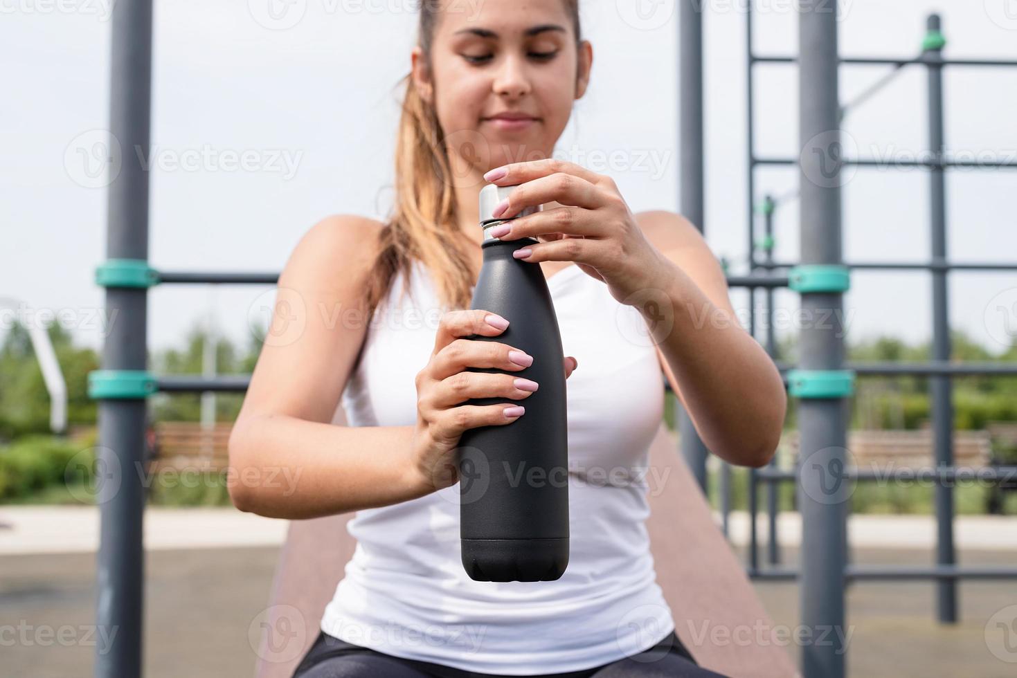 gelukkige vrouw die op het sportveld traint op een zonnige zomerdag, drinkt water uit de fles foto