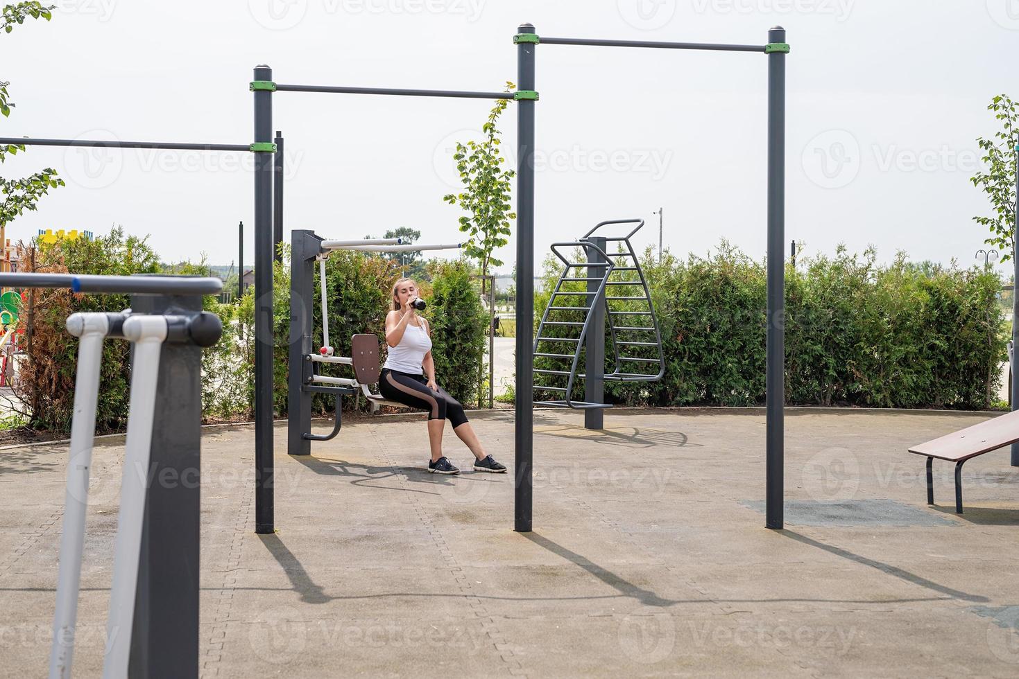 gelukkige vrouw die op het sportveld traint op een zonnige zomerdag, drinkt water uit de fles foto