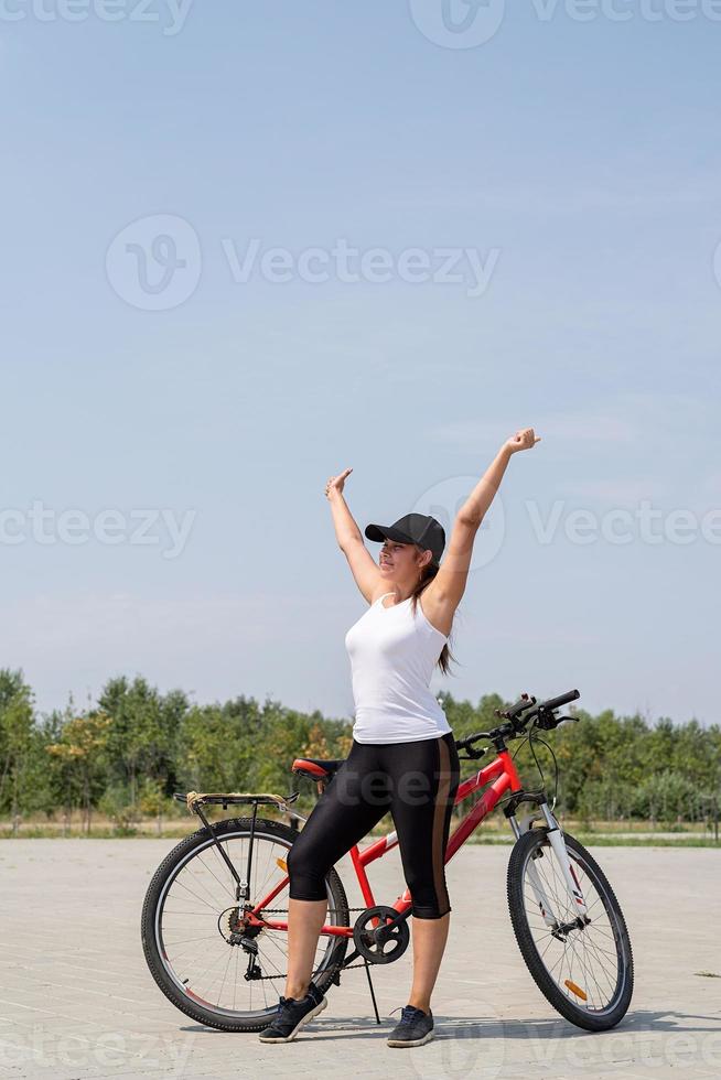 gelukkige vrouw met opgeheven armen staande bij haar fiets in een park met rust, volbracht haar reis foto