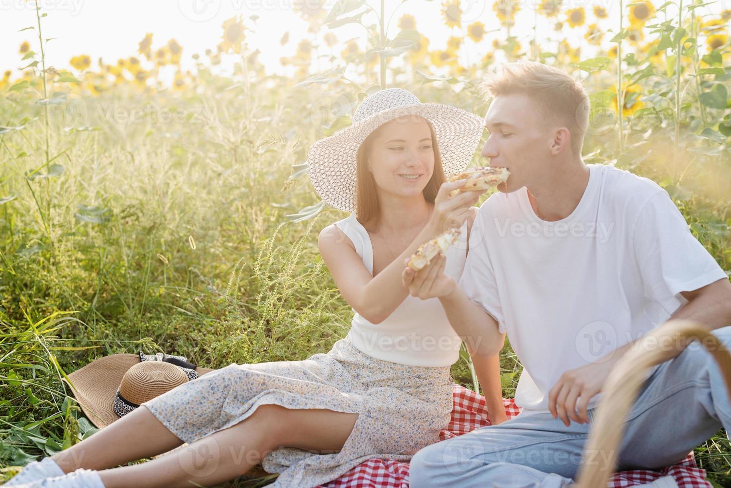 jong koppel met picknick op zonnebloemveld bij zonsondergang foto