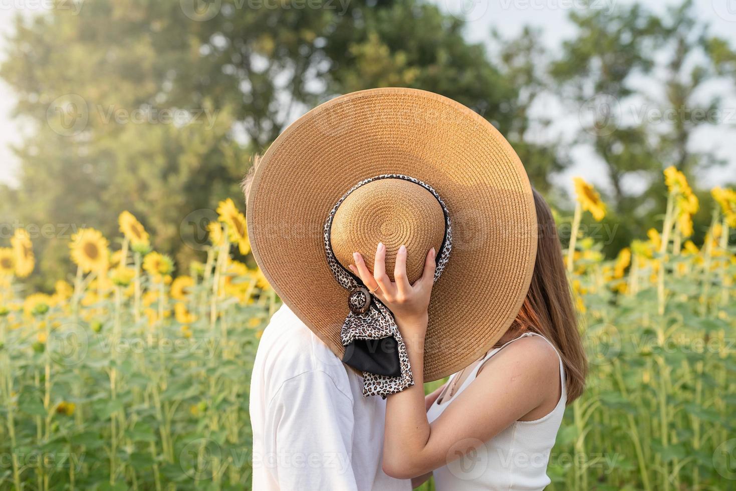 jonge gelukkige paar zoenen op een picknickdeken, hun gezichten bedekken met een zomerhoed foto