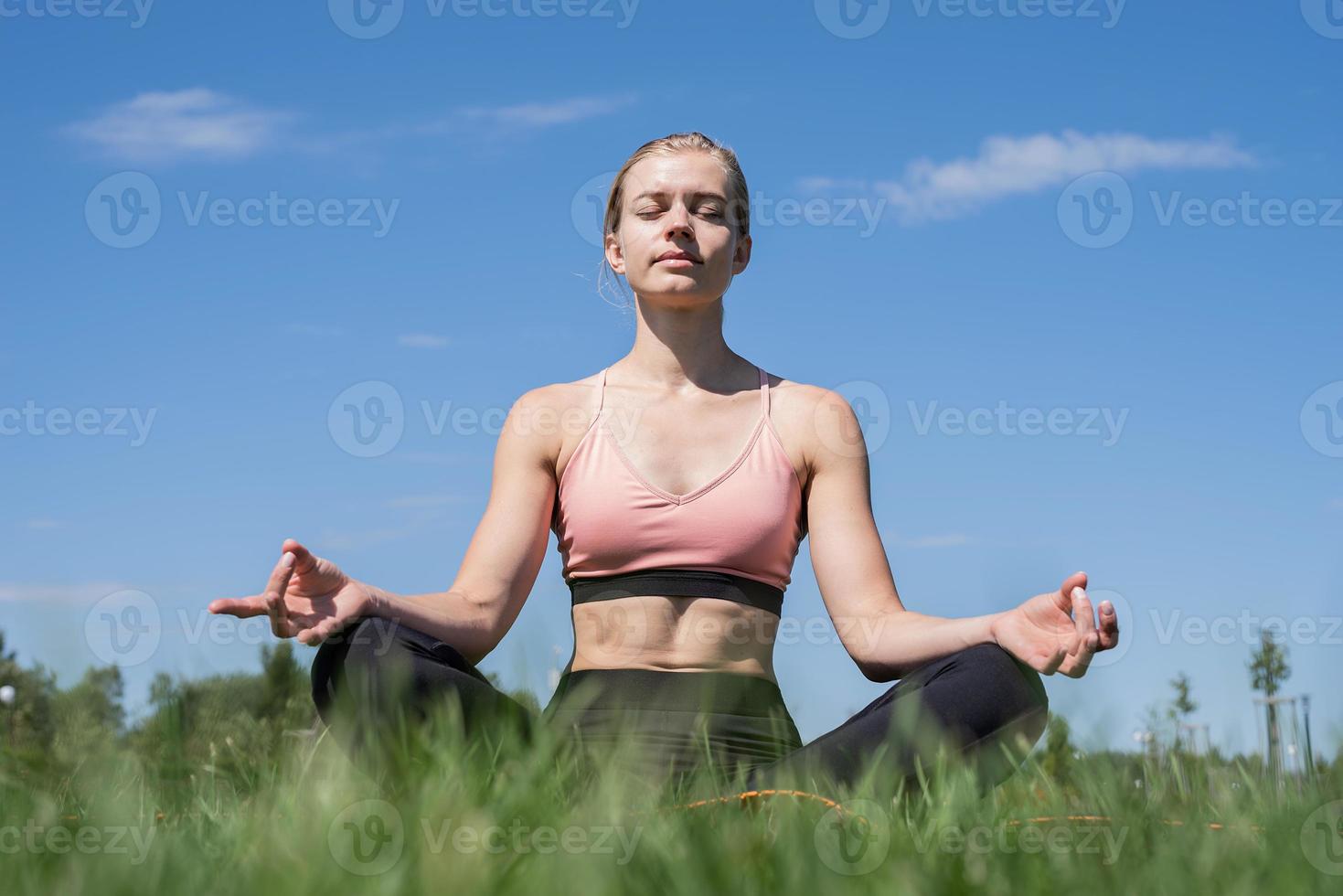 sportieve vrouw mediteren zittend op gras onder blauwe hemel foto