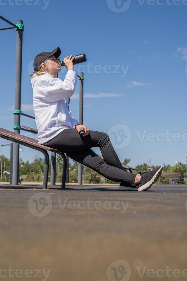 jonge sportieve vrouw in sporthandschoenen drinkwater op sportterrein foto