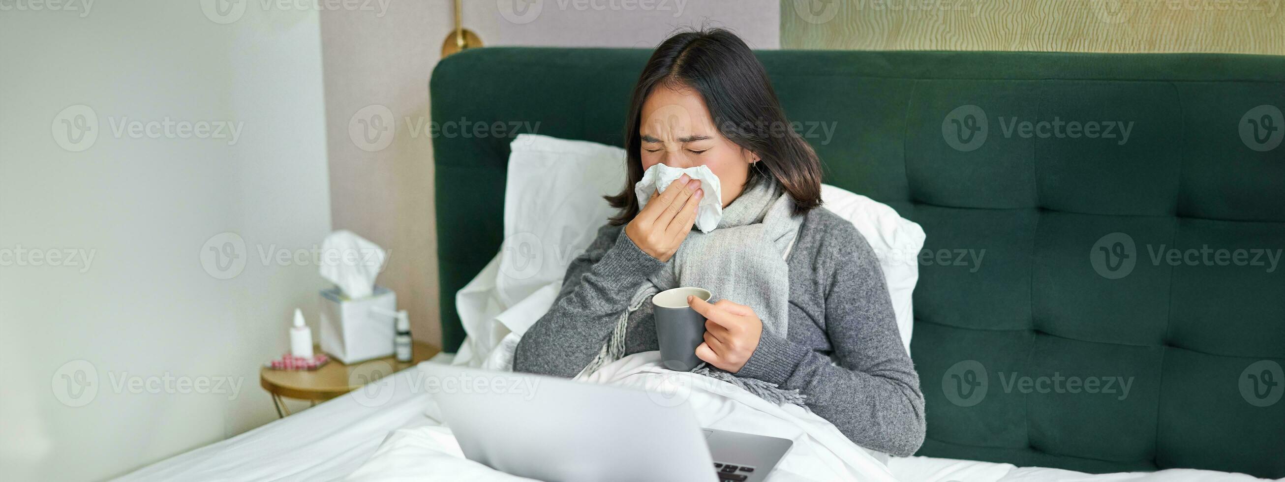 vrouw met koud, hebben griep, blijven in bed, niezen in servet, vloeibaar neus- en influenza symptomen foto