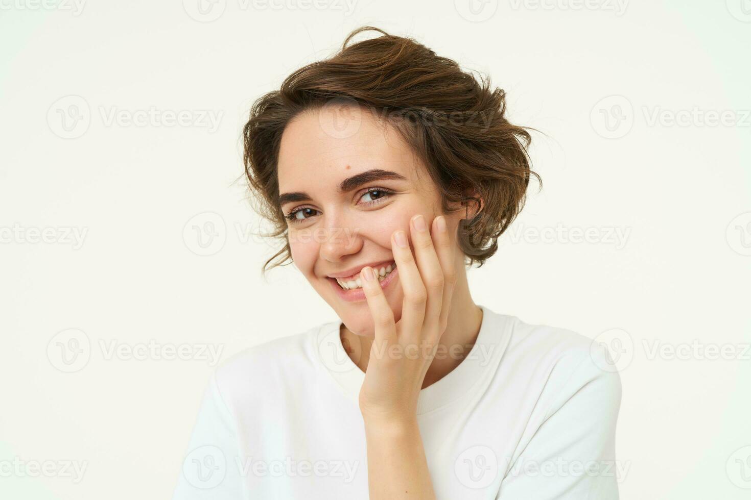 portret van brunette vrouw lachend, glimlachen en aan het bedekken gezicht met hand, op zoek verlegen en schattig, staand over- wit achtergrond foto