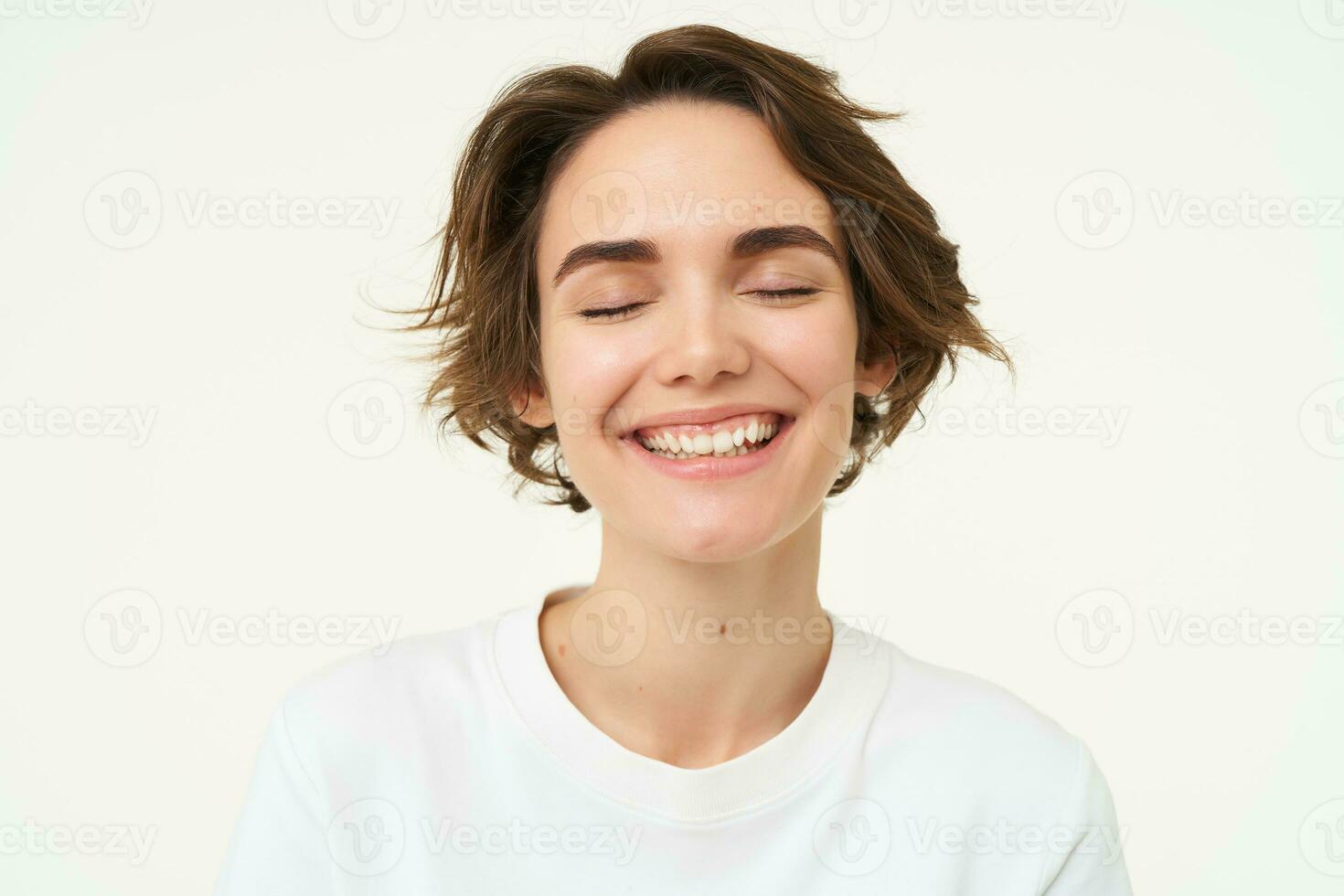 dichtbij omhoog portret van brunette meisje met kort kapsel, glimlachen en op zoek Vrolijk, poseren over- wit achtergrond foto