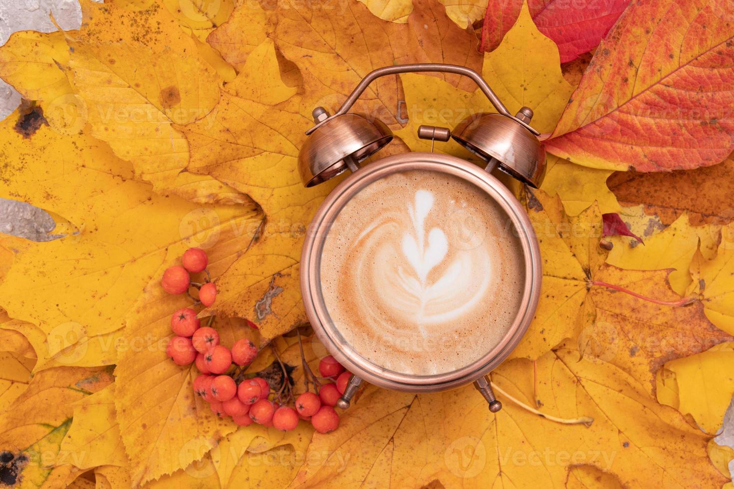 koffiekunst in een wekker op een achtergrond van gevallen bladeren. herfsttijd en koffie in de ochtend foto