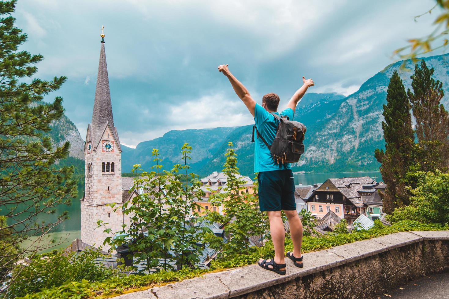 gelukkige man toerist die staat met opstaande handen en kijkt naar de stad Hallstatt van bovenaf foto