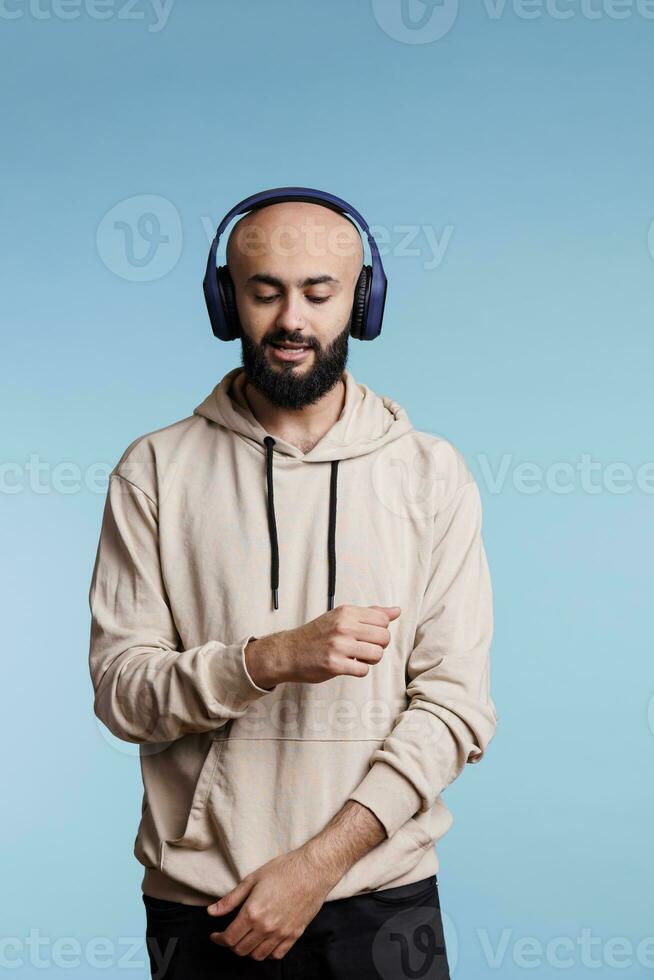 Arabisch Mens dansen, gevoel ritme en genieten van muziek- in koptelefoon. jong kaal gebaard persoon vervelend gewoontjes capuchon luisteren naar liedjes afspeellijst in draadloze oortelefoons en in beweging handen foto