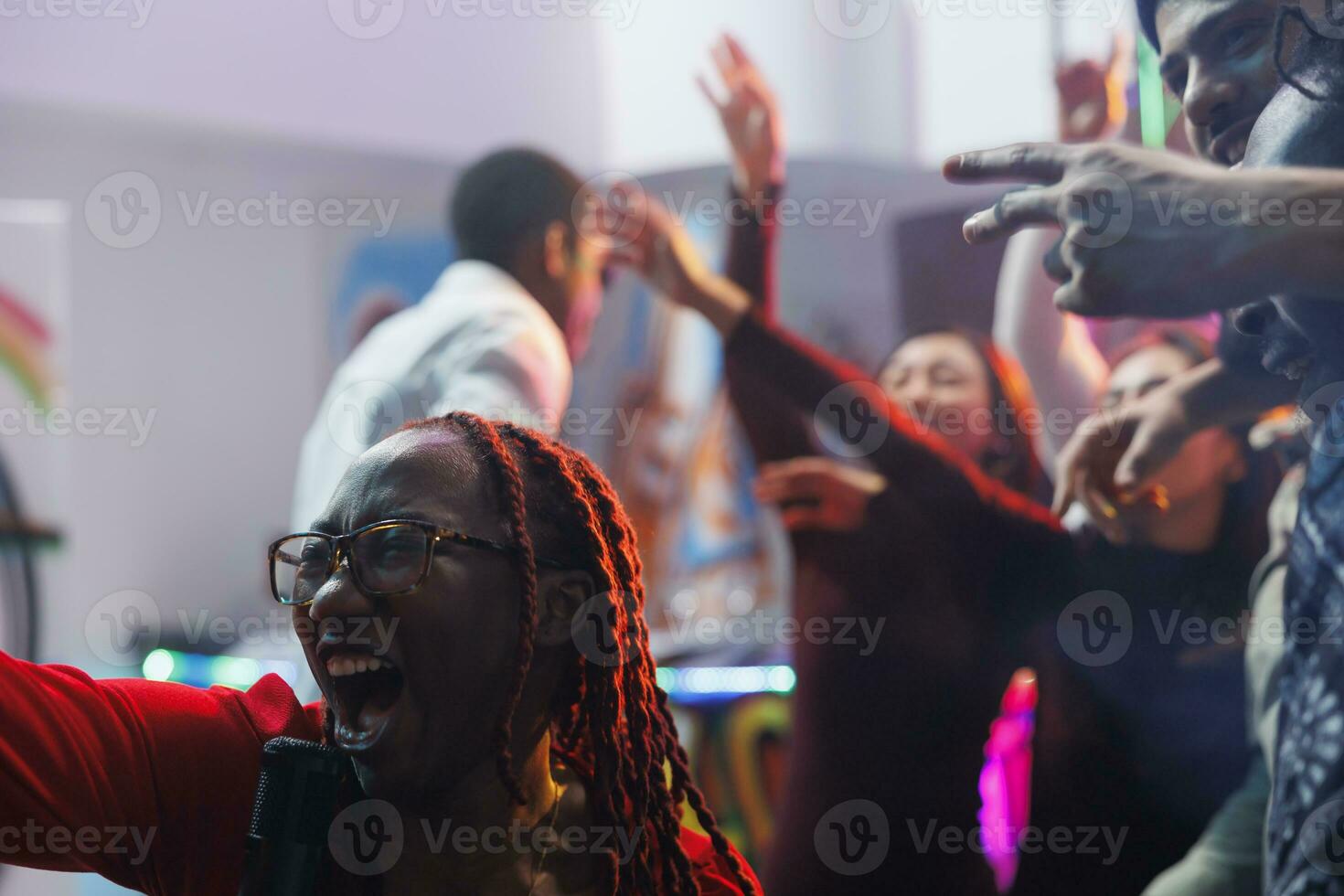 vrouw het zingen in microfoon luid en schreeuwen terwijl feesten met vrienden in nachtclub. zorgeloos Afrikaanse Amerikaans clubber geschreeuw terwijl hebben pret en genieten van karaoke in club foto