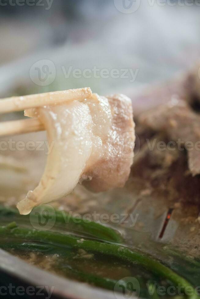 gebruik eetstokjes naar plukken omhoog de varkensvlees buik plakjes van pot naar eten foto