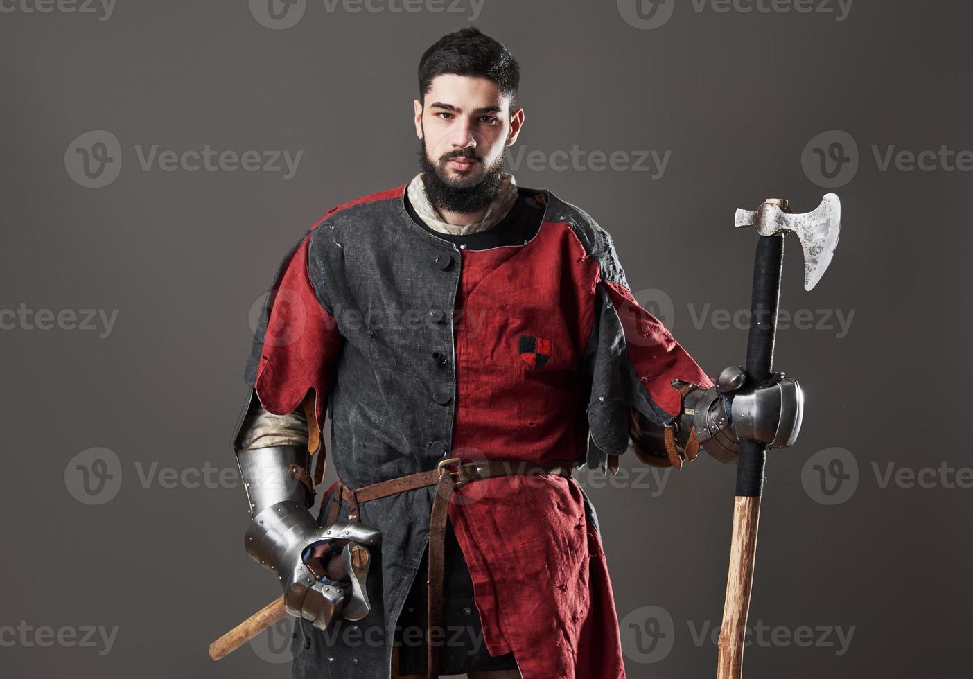 middeleeuwse ridder op grijze achtergrond. portret van brutale vuile gezichtskrijger met maliënkolder, rode en zwarte kleding en strijdbijl foto