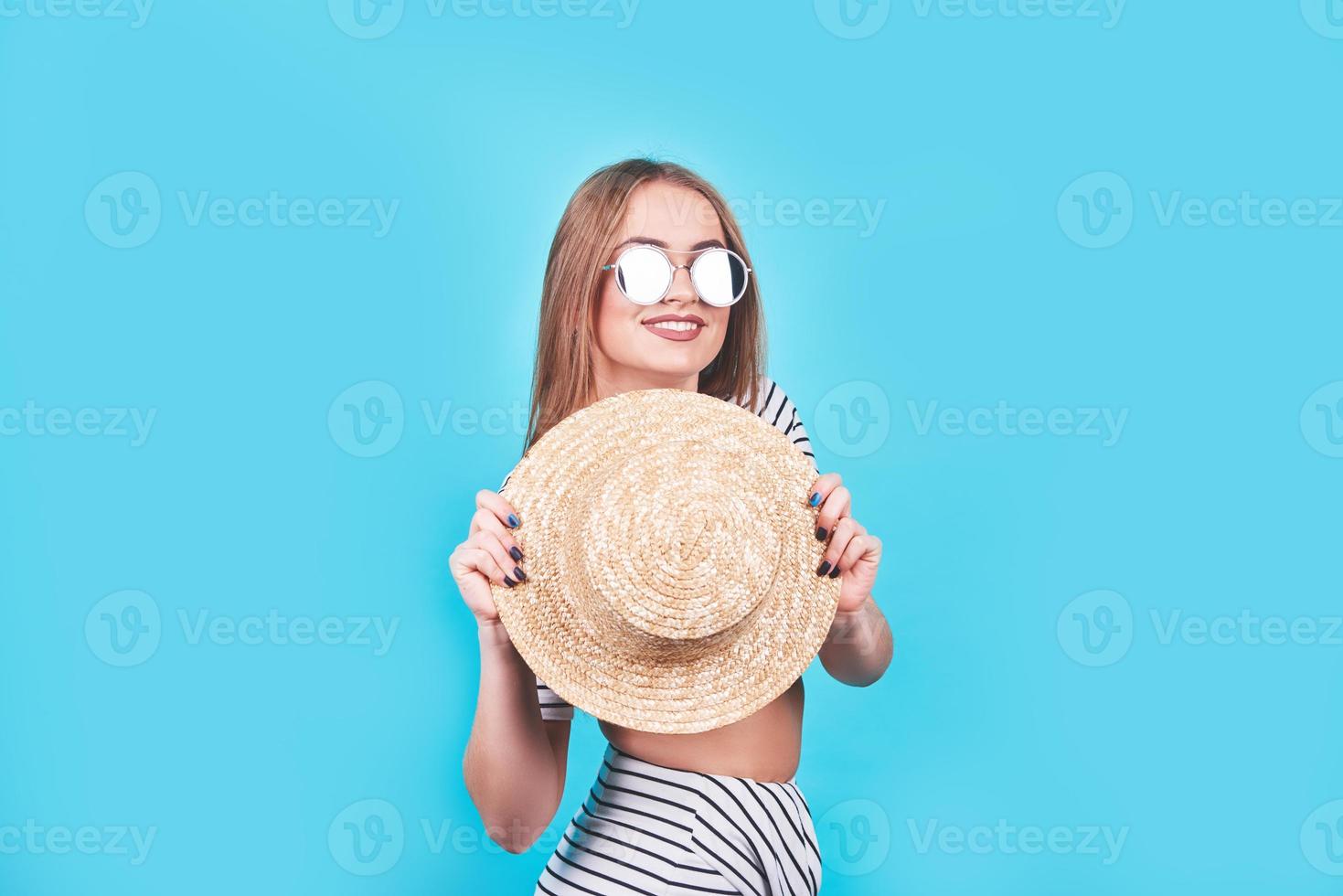 aantrekkelijk meisje in een witte en zwarte strepen, hoed, zonnebril, emotioneel geopende mond op een helderblauwe achtergrond met een perfect lichaam. geïsoleerd. studio opname foto