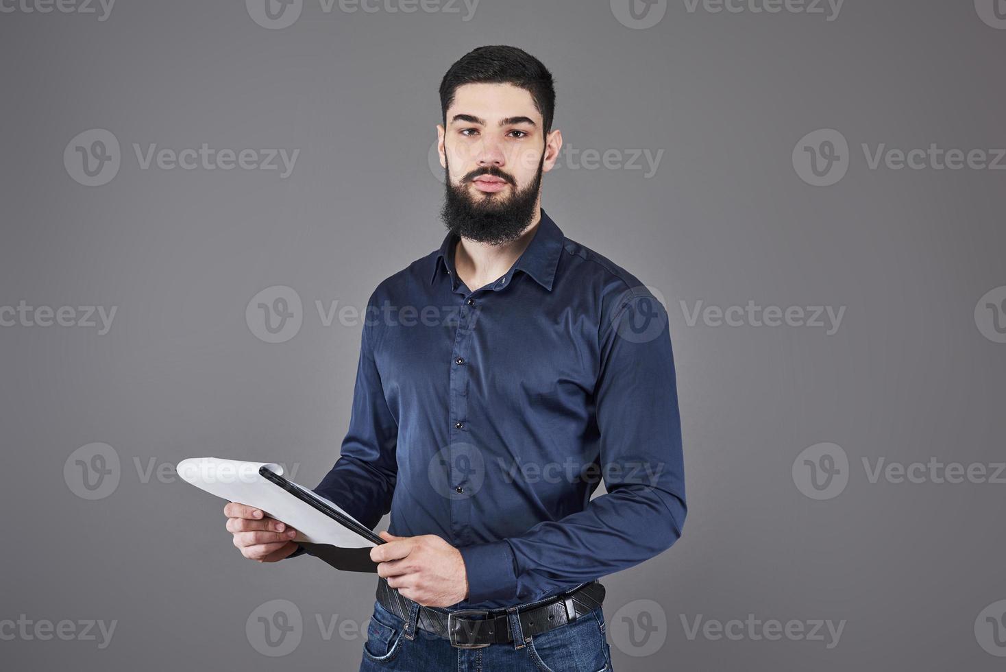 geconcentreerde jonge aantrekkelijke zakenman in blauw shirt plannen en schrijven in klembord foto