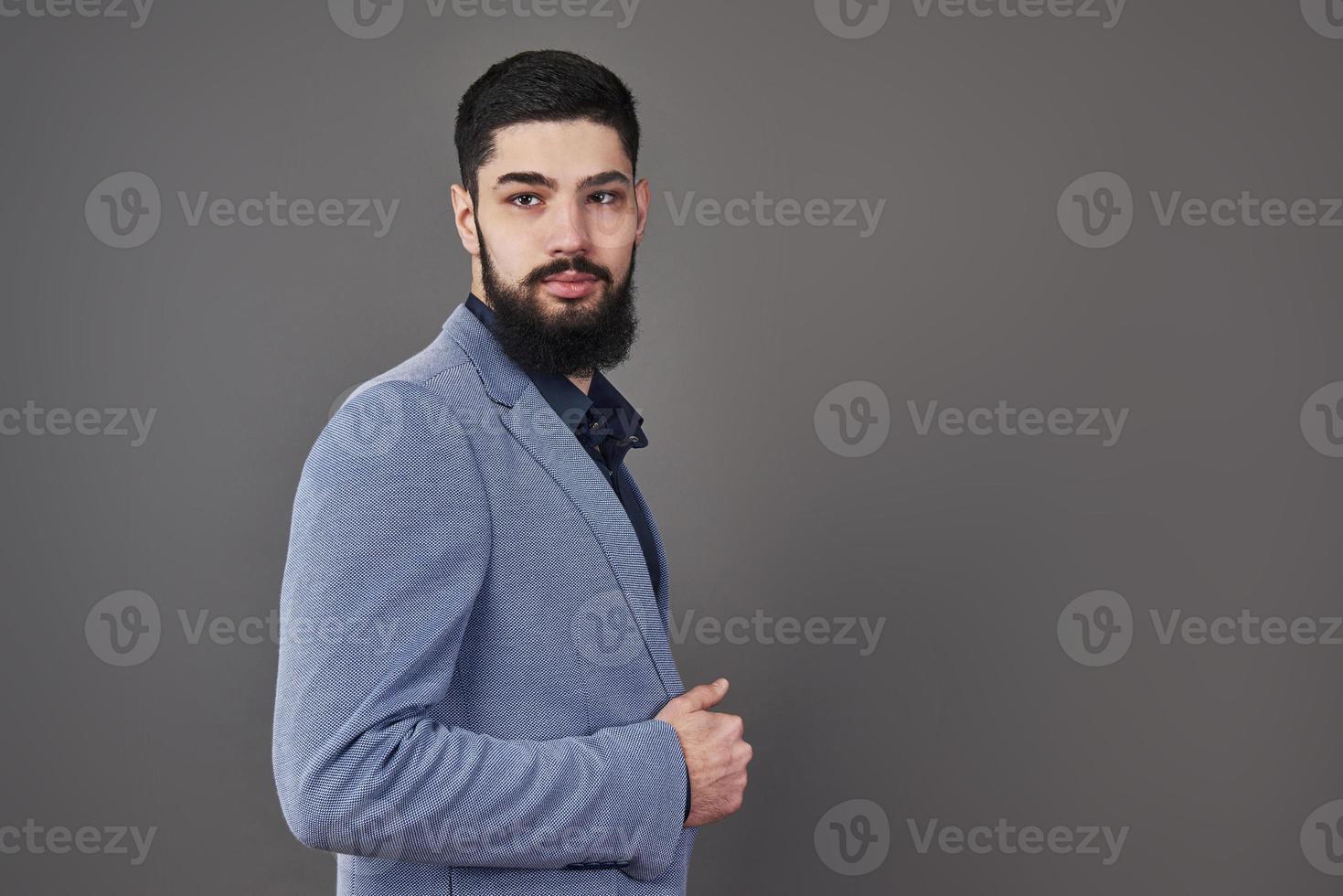 portret van freelancer man met baard in jas staande tegen een grijze achtergrond foto