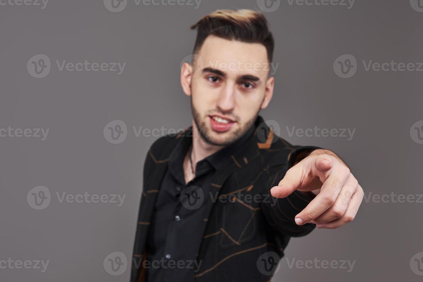 Glimlachende jongeman in formele kleding wijzend met de vinger op je, kijkend naar de camera, geïsoleerd op een grijze achtergrond foto