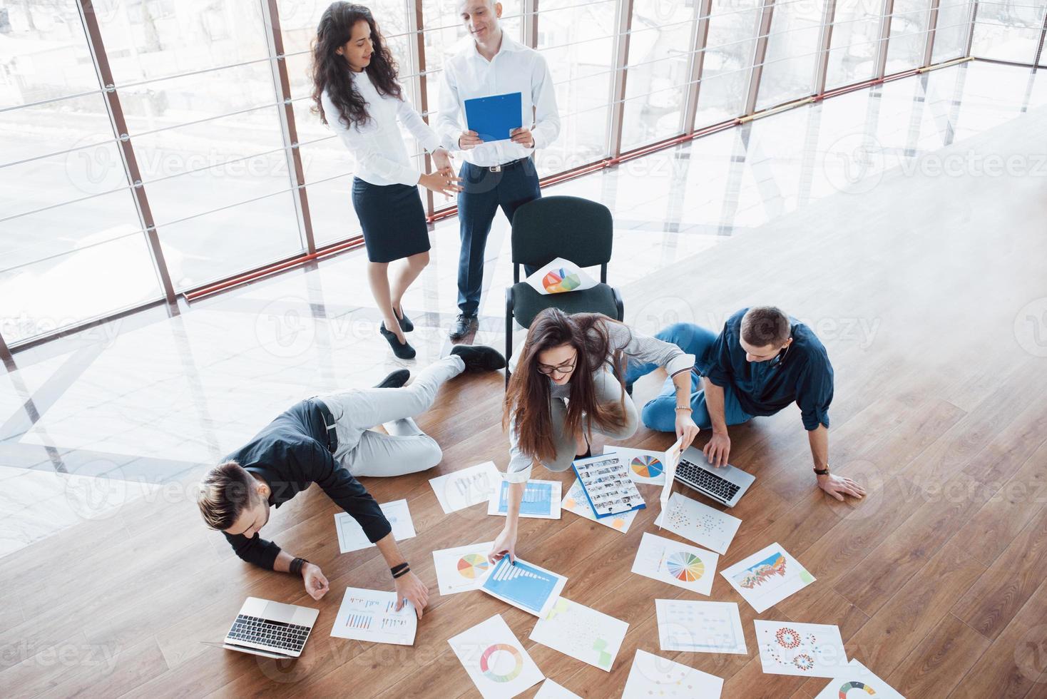 planningsstrategie samen. business team kijkt naar papieren op de vloer met manager die naar één idee wijst. samenwerking corporate prestatie. planning ontwerp tekenen. teamwork concept foto