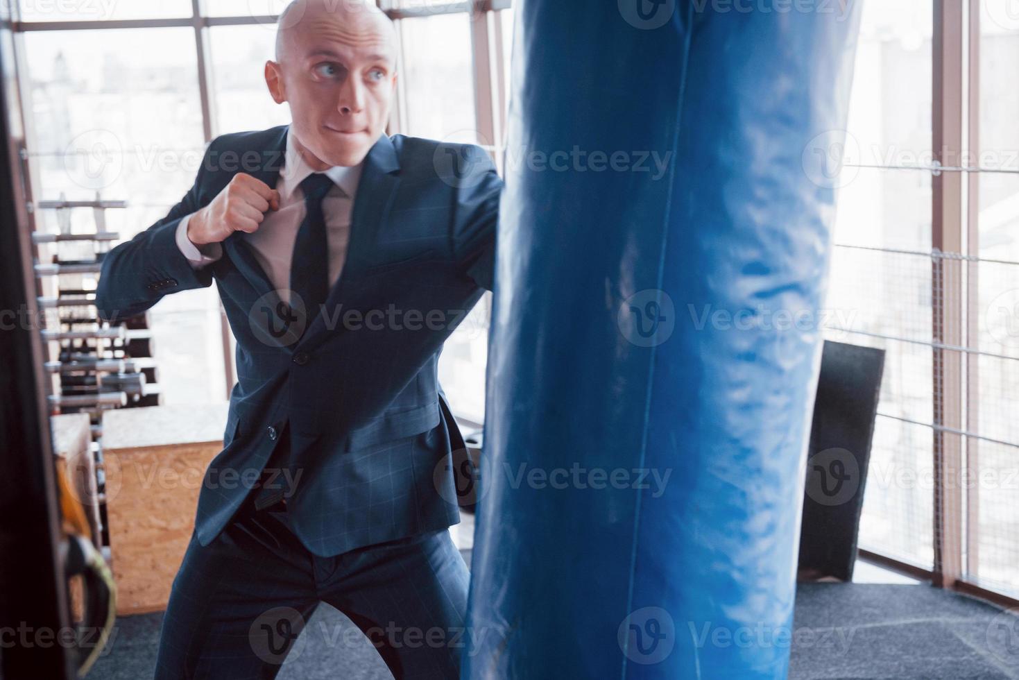 een boze kale zakenman verslaat een bokspeer in de sportschool. concept van woedebeheersing foto