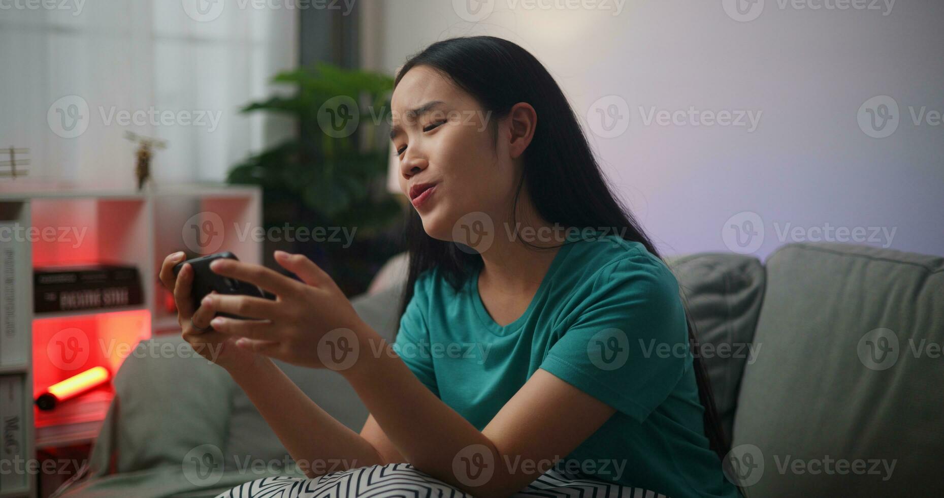 portret van jong Aziatisch vrouw geniet spelen online esport spellen Aan smartphone zittend Aan sofa in de leven kamer Bij thuis, gamer levensstijl concept, gamer levensstijl concept. foto