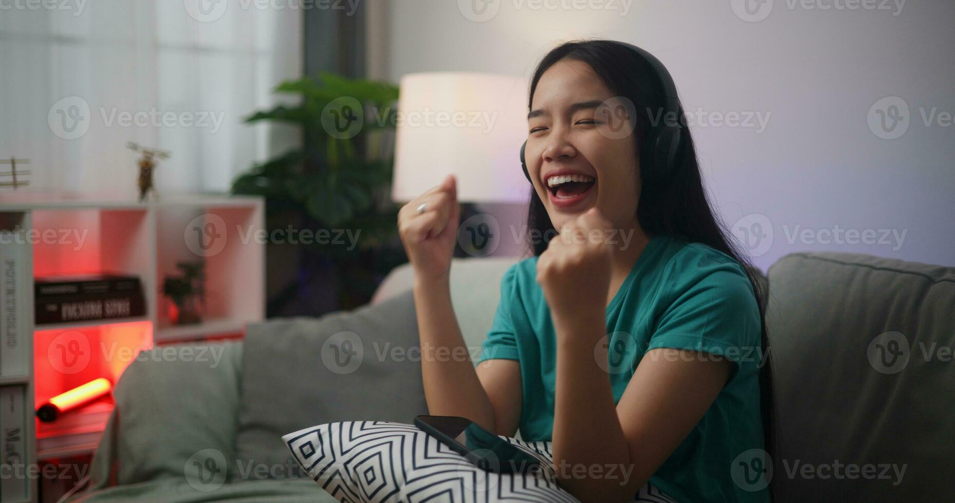portret van jong Aziatisch vrouw vervelend bril en hoofdtelefoons geniet spelen online esport spellen Aan smartphone zittend Aan sofa in de leven kamer Bij thuis, gamer levensstijl concept. foto