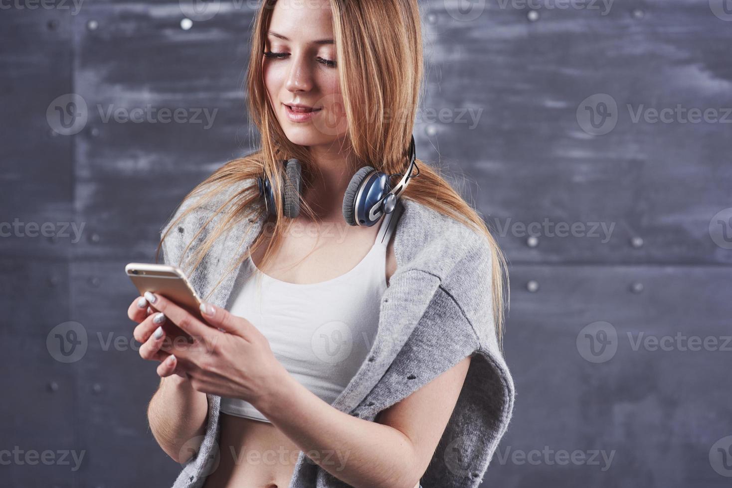 headshot van jonge schattige blonde vrouw met schattige glimlach die grote zwarte professionele monitoring-koptelefoons draagt tegen een grijze studio-achtergrond foto
