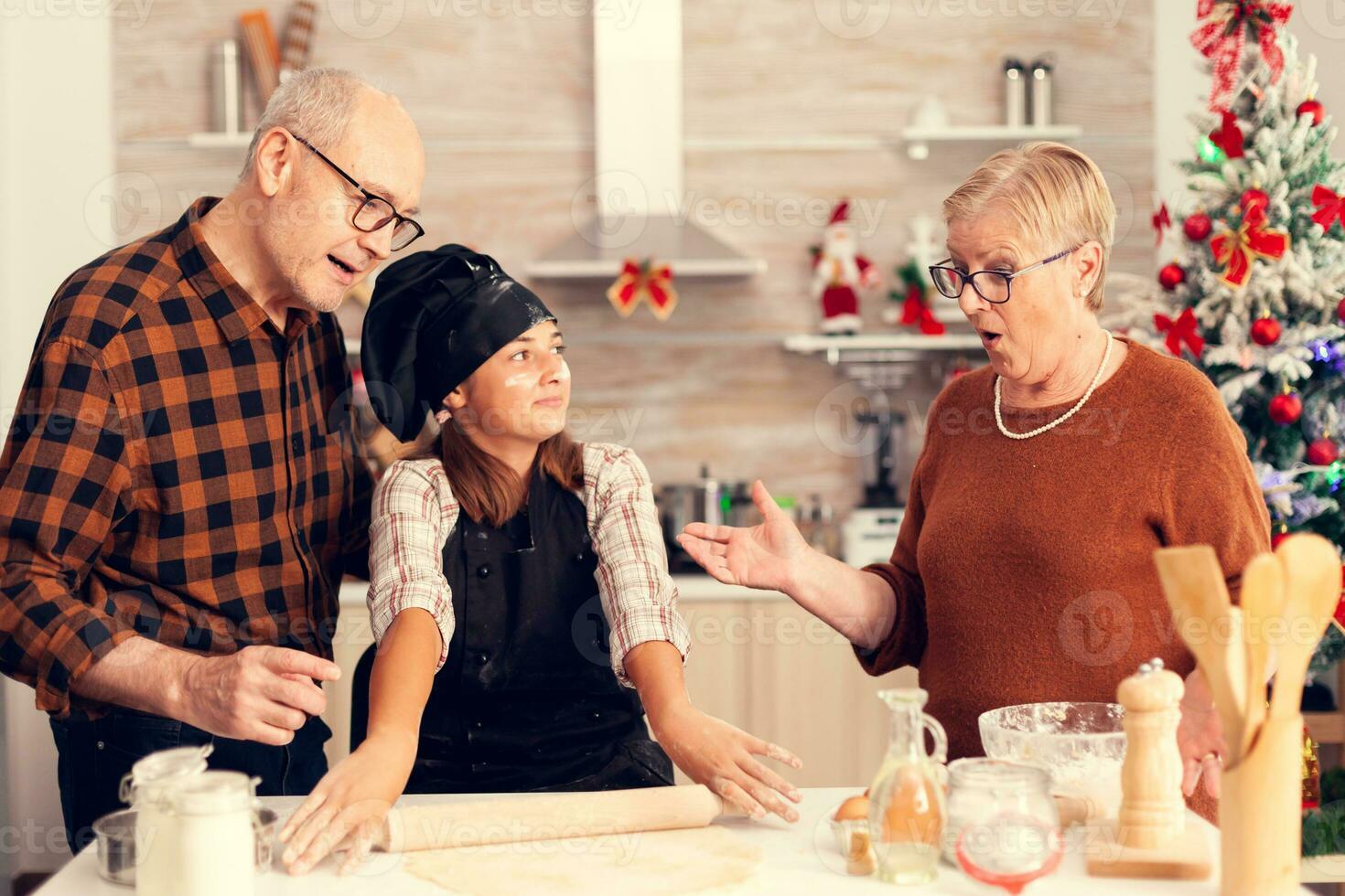 kind verrassend grootouder Aan Kerstmis dag maken nagerecht. gelukkig vrolijk vrolijk tiener- meisje helpen senior vrouw voorbereidingen treffen zoet koekjes naar vieren winter vakantie. foto