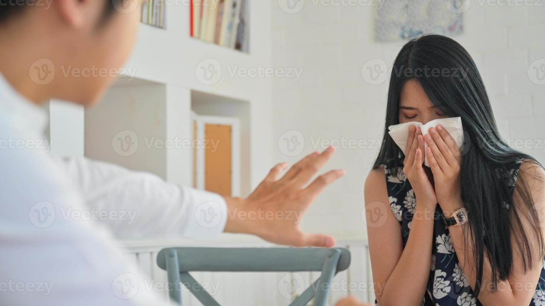 een jonge vrouw die niest tijdens het werken met een mannelijke partner. hij was doodsbang voor covid-19. foto