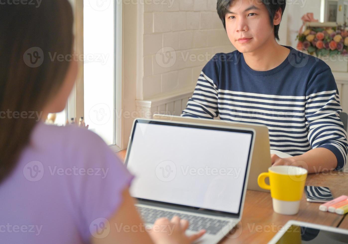 jonge vrouwelijke student gebruikt een laptop en adviseert een mannelijke student die tegenover zit. ze studeren thuis online. foto