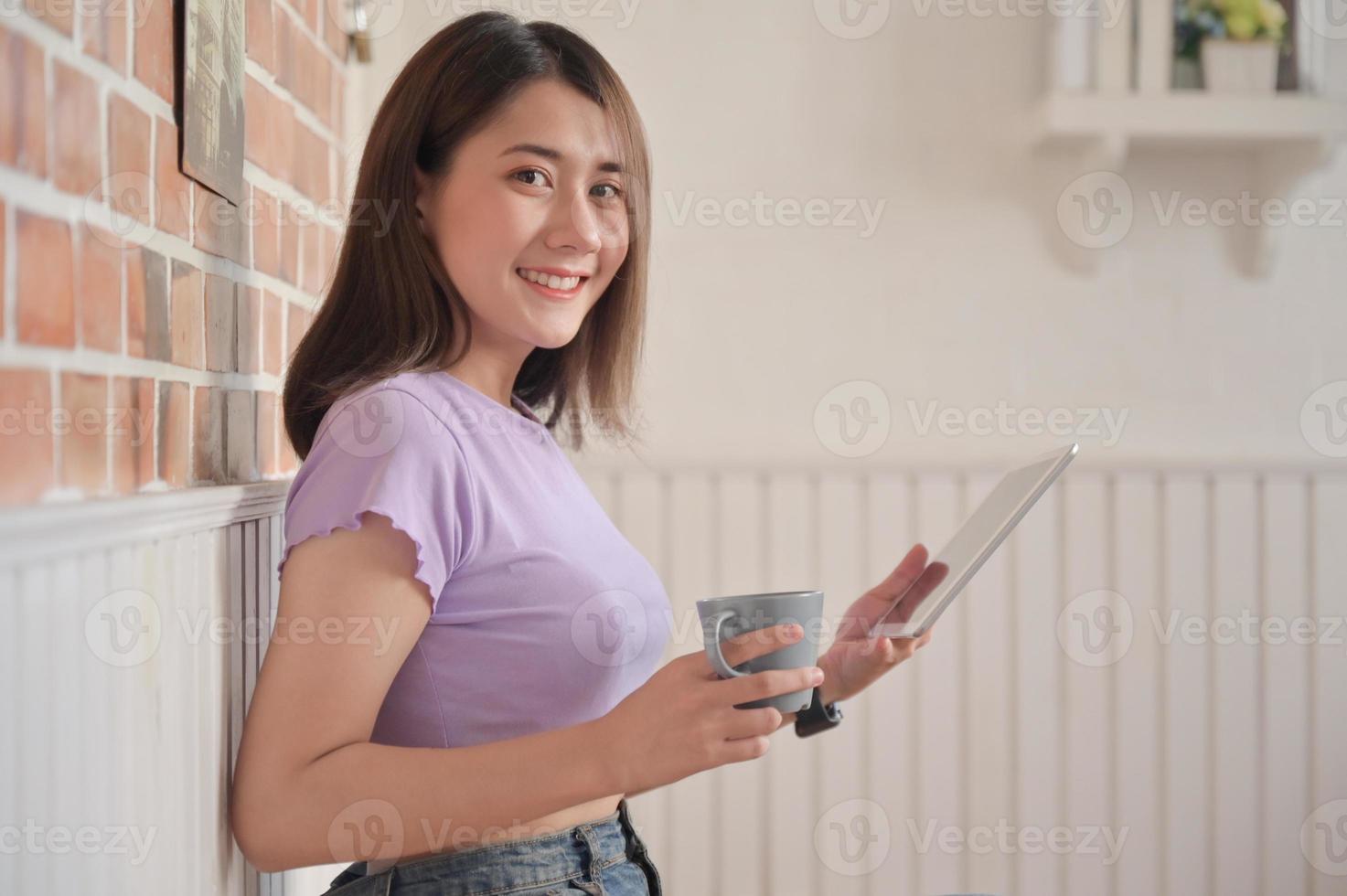 jonge vrouwelijke student met koffie die comfortabel zit, gebruikte een tablet voor videobellen met vrienden thuis. foto