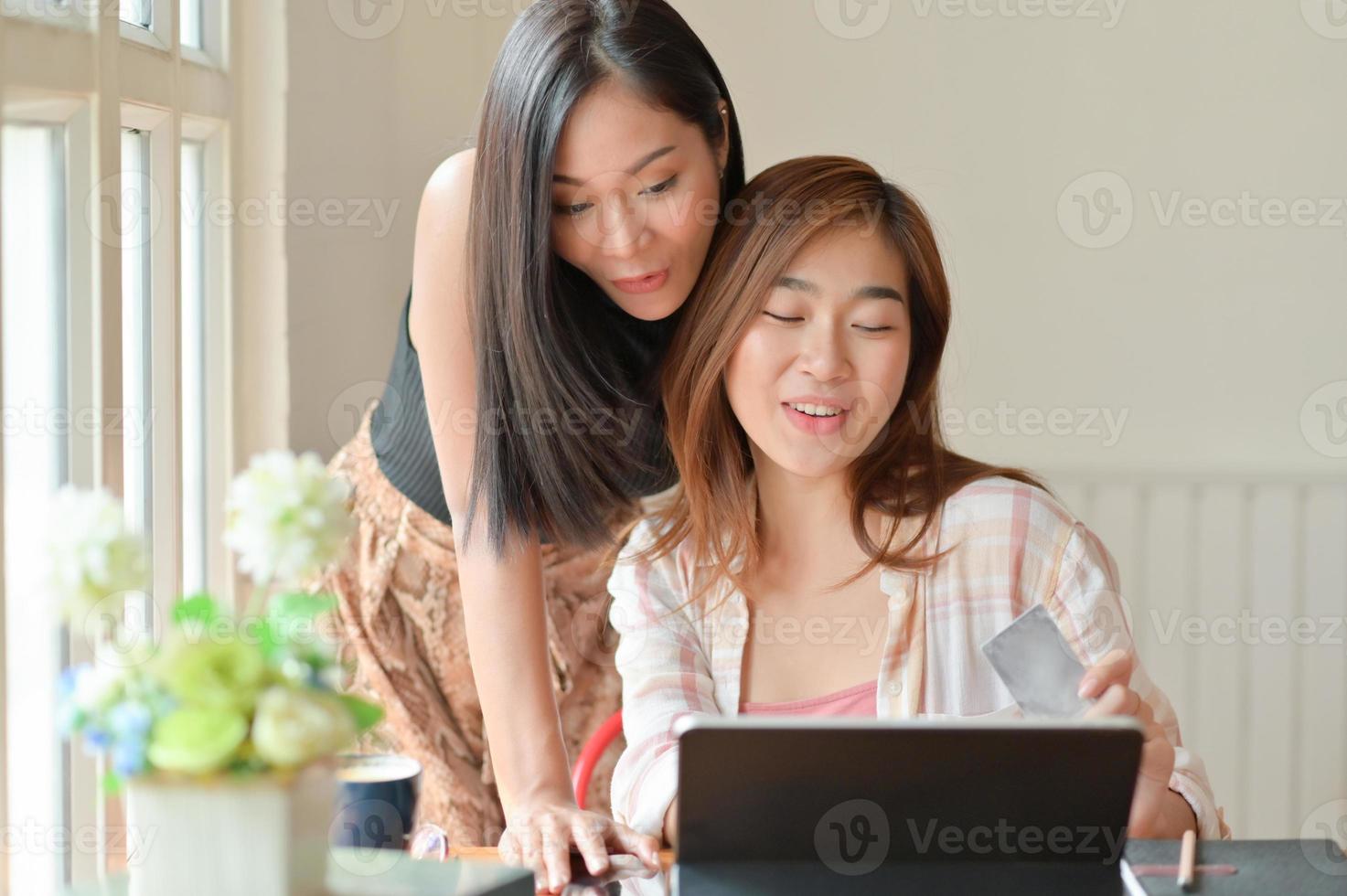 twee aziatische vrouwen hebben een creditcard en gebruiken een laptop om winkelinformatie te zoeken. foto