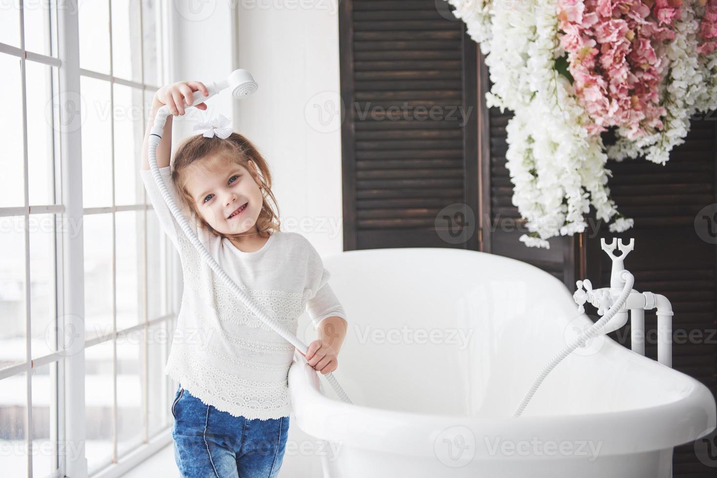 grappig klein babymeisje met krullend haar. maak je klaar om in bad te gaan. ruime verlichte badkamer. het concept van een gezond en schoon lichaam. voor jezelf zorgen sinds je kindertijd foto