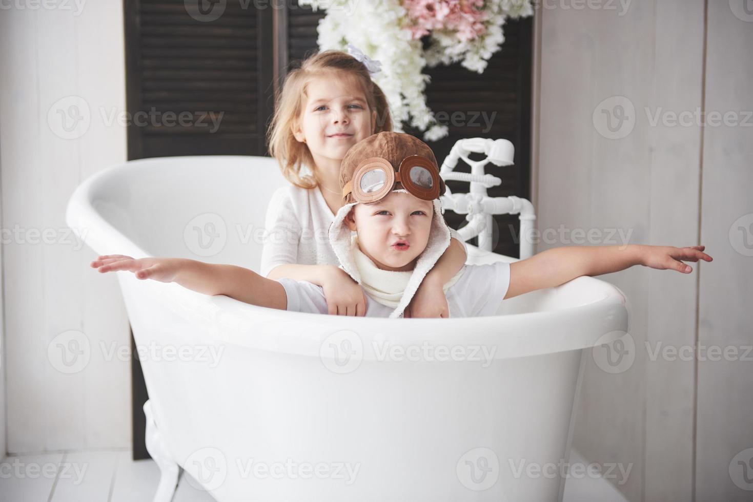 portret van een meisje en een jongen in pilotenhoed die in de badkamer spelen bij piloten of matrozen. het concept van reizen, kindertijd en de realisatie van dromen foto