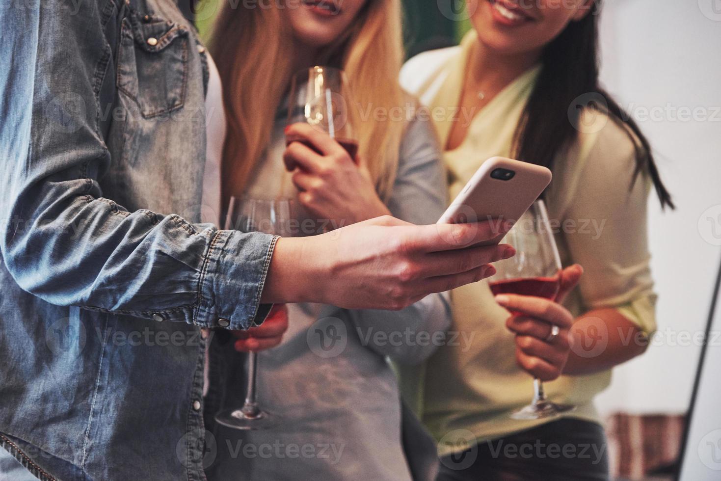 foto van een gelukkige groep vriendinnen met rode wijn. samen zien ze een foto op een smartphone