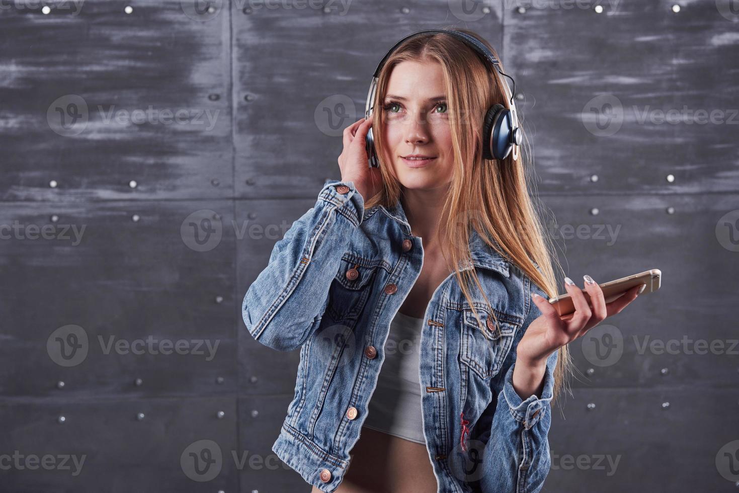 mode, kleding, mensen concept. aantrekkelijke sexy jonge vrouw met jeans jasje. meisje poseert in de studio luistert naar muziek in een koptelefoon foto