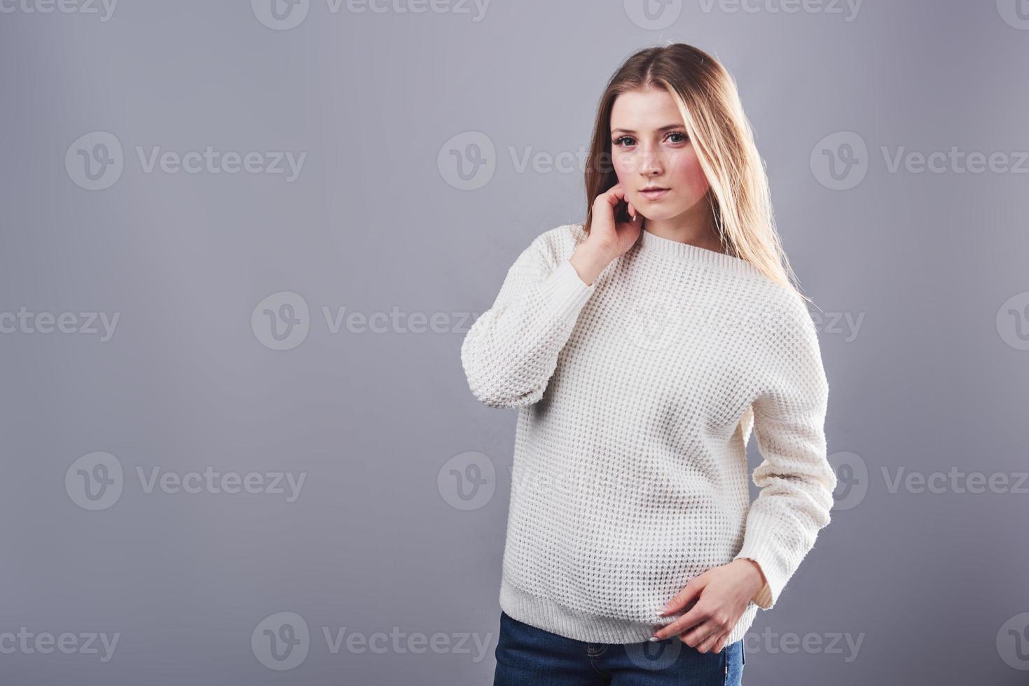 portret van mooie jonge vrouw in witte trui en jeans, geïsoleerd op een grijze achtergrond foto