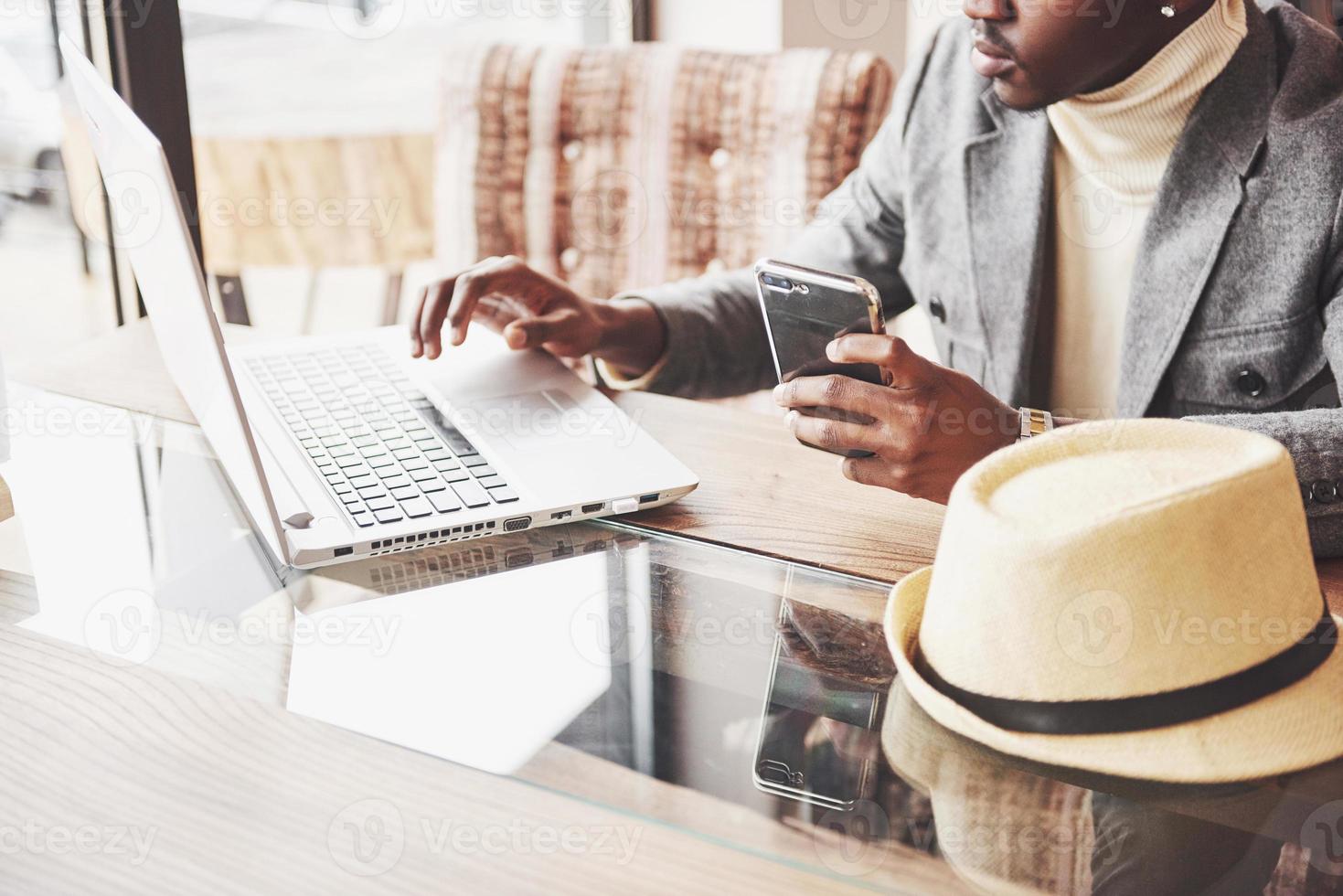 peinzende afro-amerikaanse knappe professionele schrijver van populaire artikelen in blog, gekleed in trendy outfit en bril, nadenkend over een nieuw verhaal, zijn script proeflezend vanuit een notitieboekje zittend in café foto