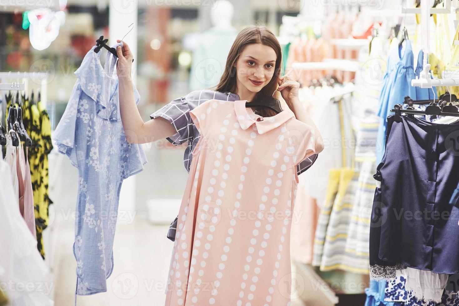 afbeelding van een jonge dame die binnenshuis in de kledingwinkel staat en jurken kiest. opzij kijken foto