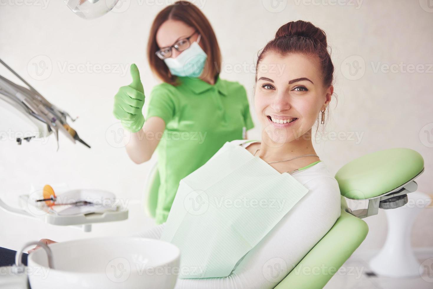 een jonge vrouw is tevreden met het werk van de tandarts en houdt haar duim omhoog foto