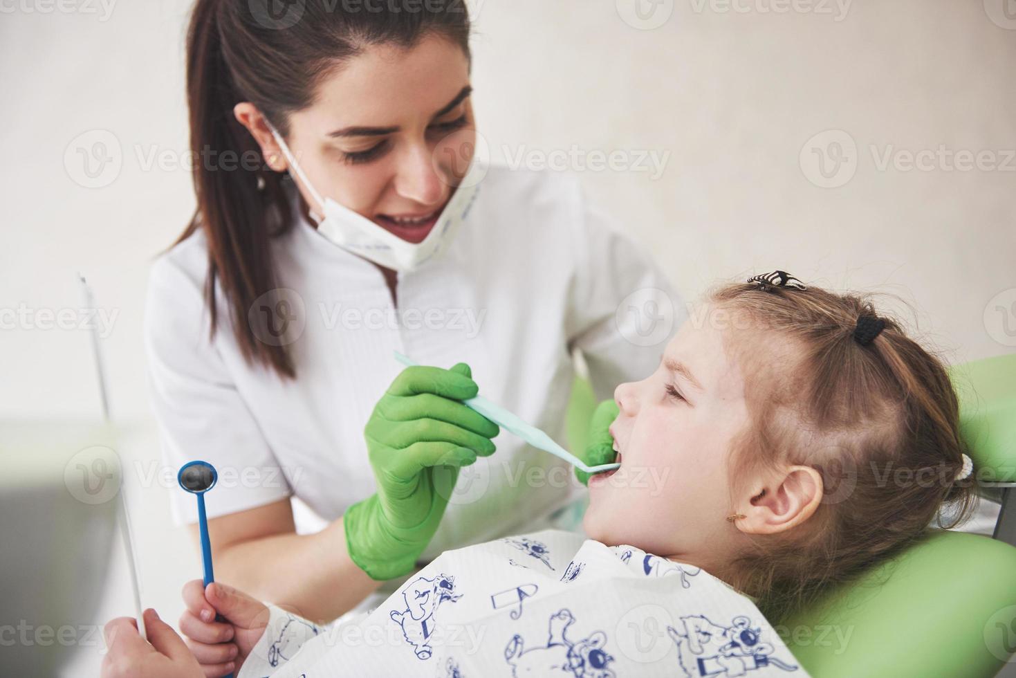 tanden check-up op het kantoor van de tandarts. tandarts die de tanden van het meisje in de tandartsstoel onderzoekt foto