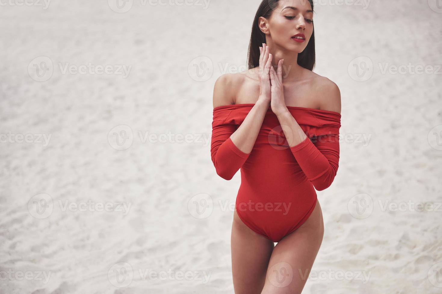 mooie jonge gebruinde vrouw in rode bikini poseren op het strand. sexy modelportret met perfect lichaam. zomervakantie concept foto