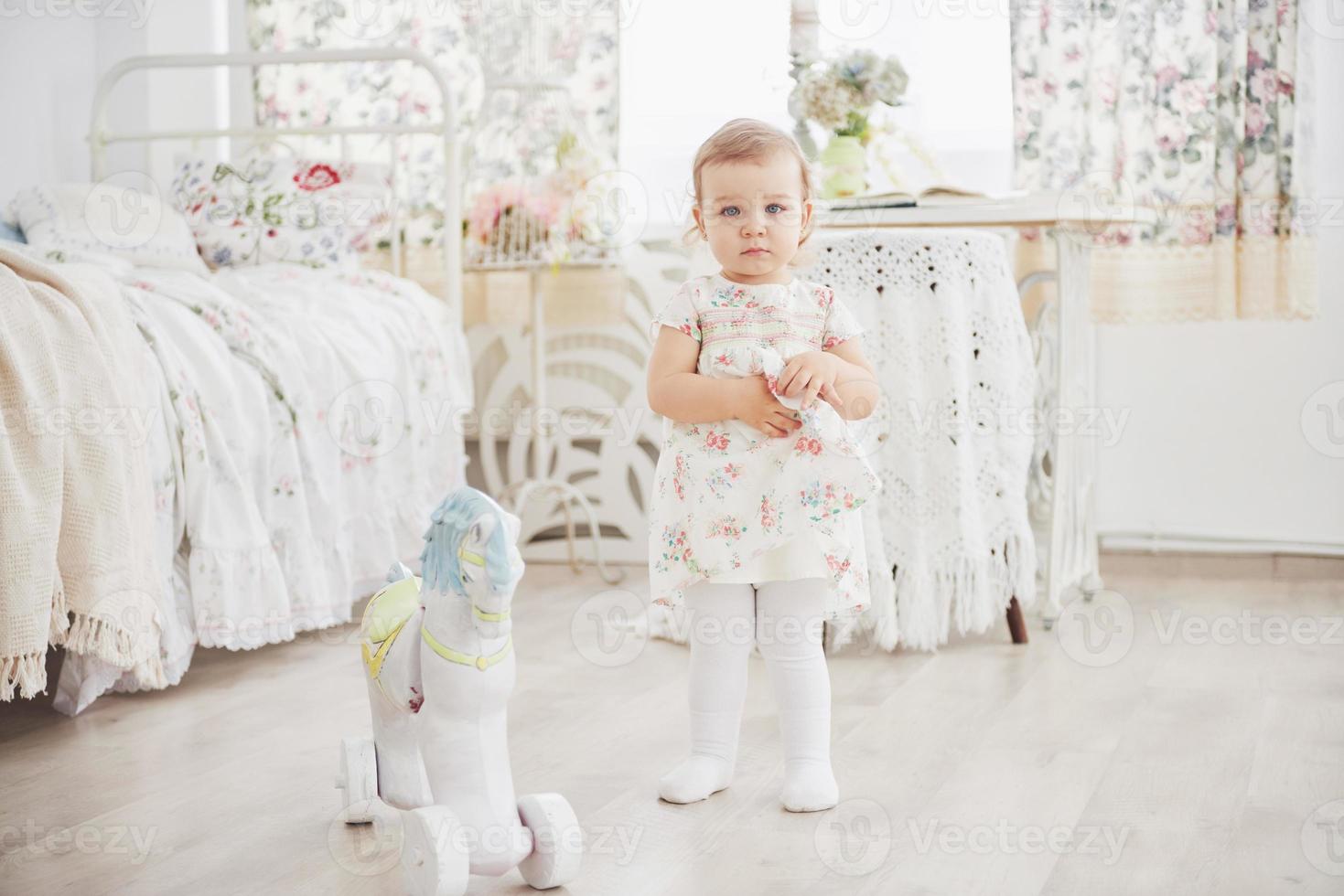 mooi klein meisje dat speelgoed speelt. blondine met blauwe ogen. witte stoel. kinderkamer. gelukkig klein meisjesportret. kindertijd concept foto