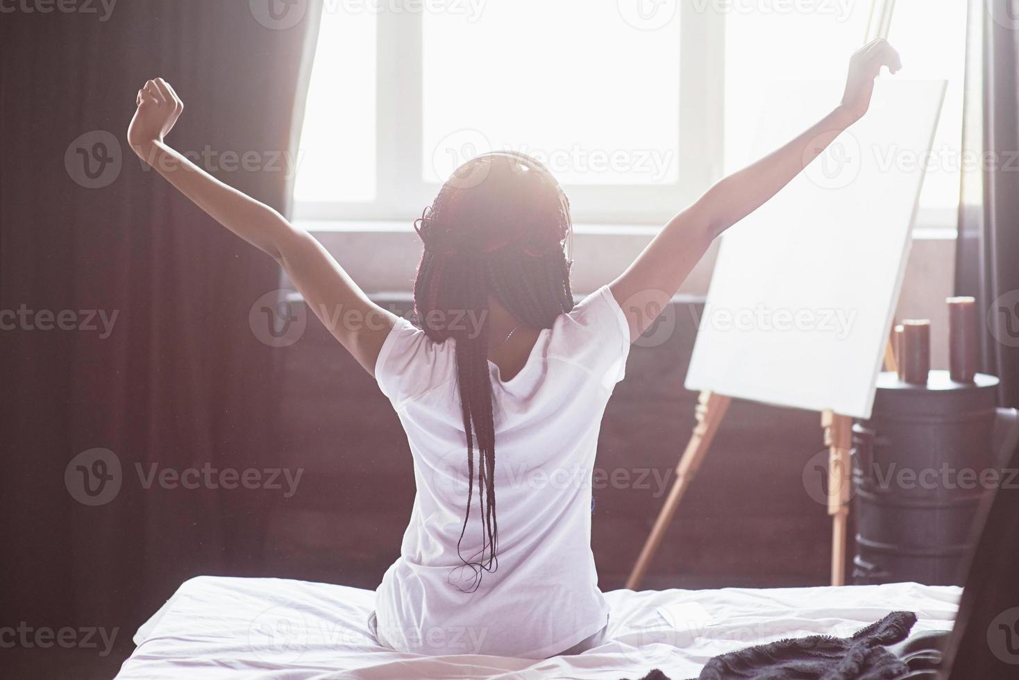 mooie zwarte vrouw die wakker wordt in haar bed, ze lacht en strekt zich uit foto